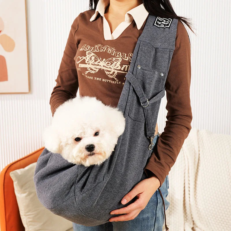 A person is holding a gray portable pet carrier sling bag with a fluffy white dog in the carrier.