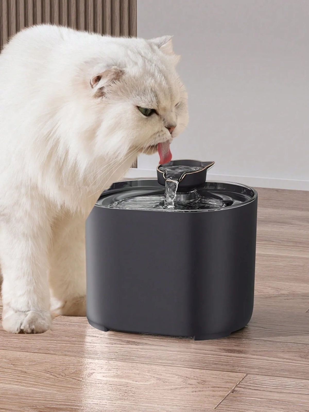 A white cat is drinking water from a modern, dark gray automatic pet water fountain.
