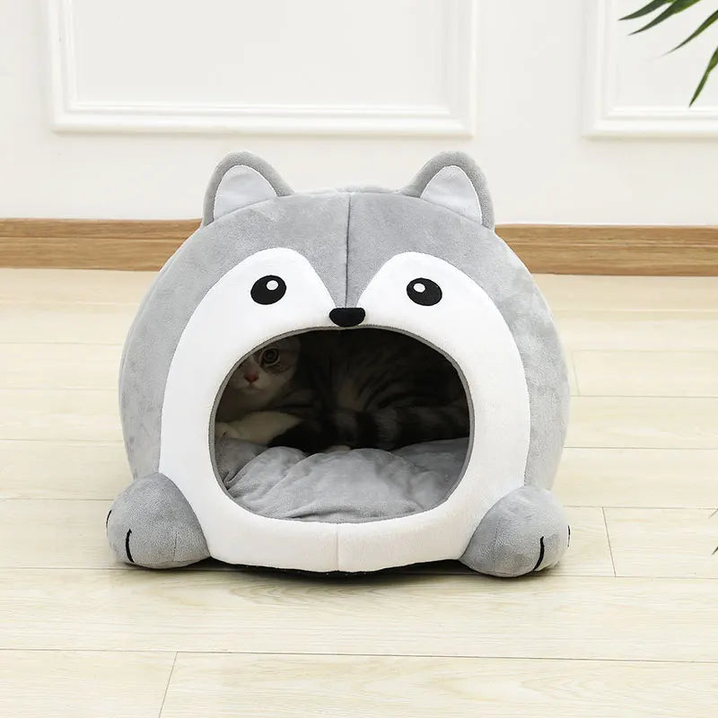 Un lit-caverne en peluche gris et blanc avec une entrée pour chaton sur un plancher en bois.