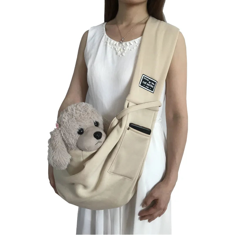 A beige portable pet carrier sling bag with a fluffy gray stuffed animal attached, worn by a person.