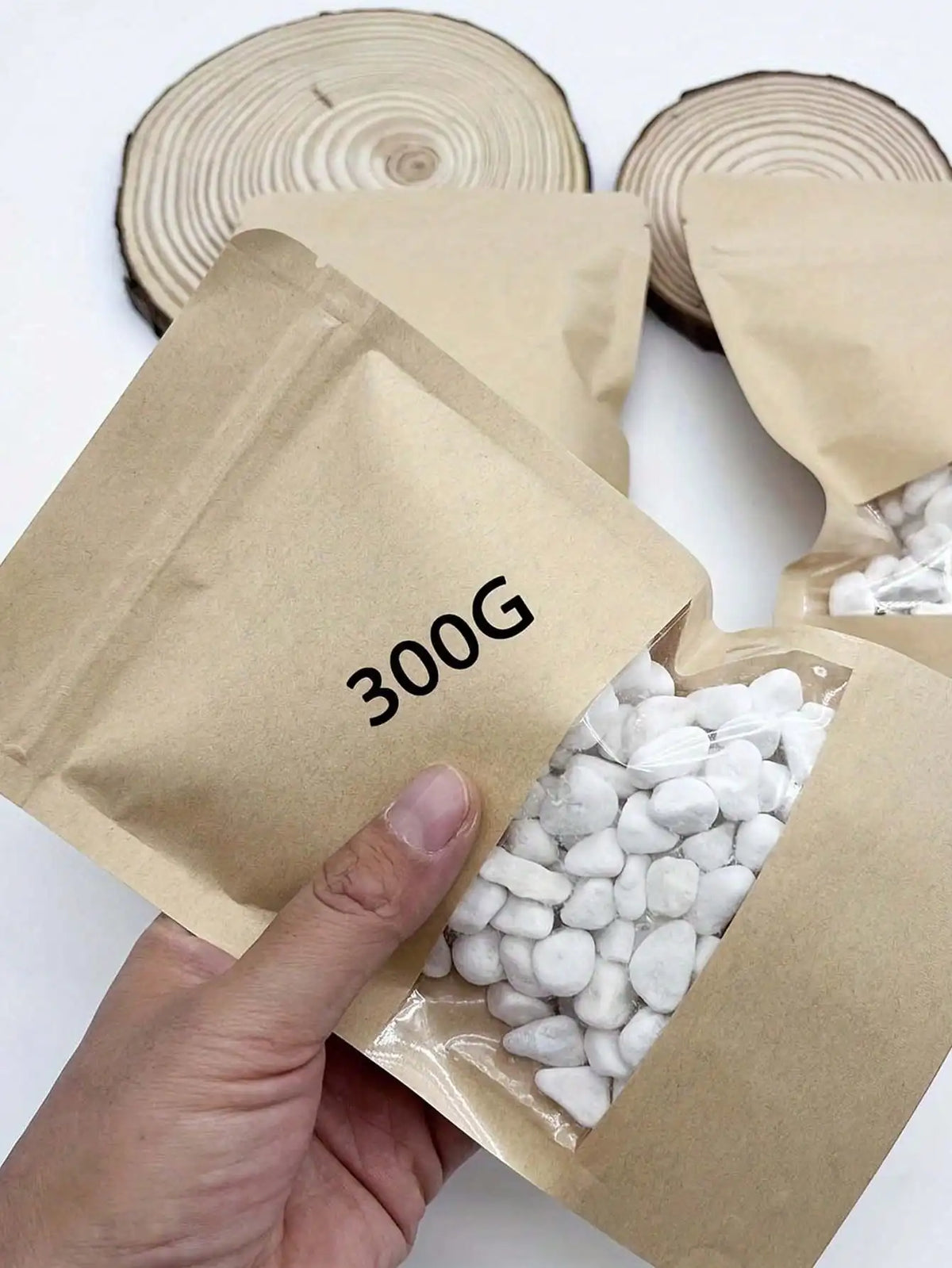 A hand holds a brown paper bag containing white pebbles for plants and landscaping.