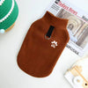A brown fleece dog sweater with a black collar and paw print embroidery is displayed next to a newspaper.