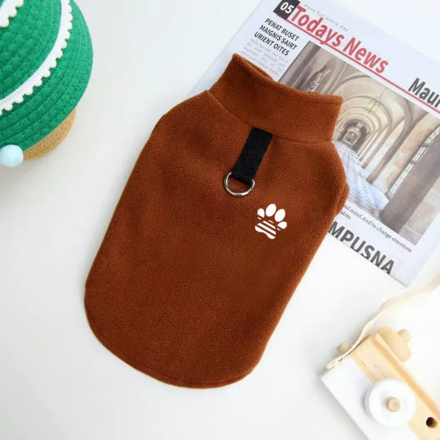 A brown fleece dog sweater with a black collar and paw print embroidery is displayed next to a newspaper.