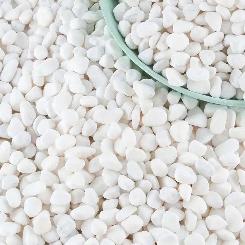 A close-up view of natural white pebbles for plants and landscaping, piled on a surface with a small green spoon.