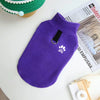 A purple fleece dog sweater with a white paw print embroidered on the chest, resting on a white surface.
