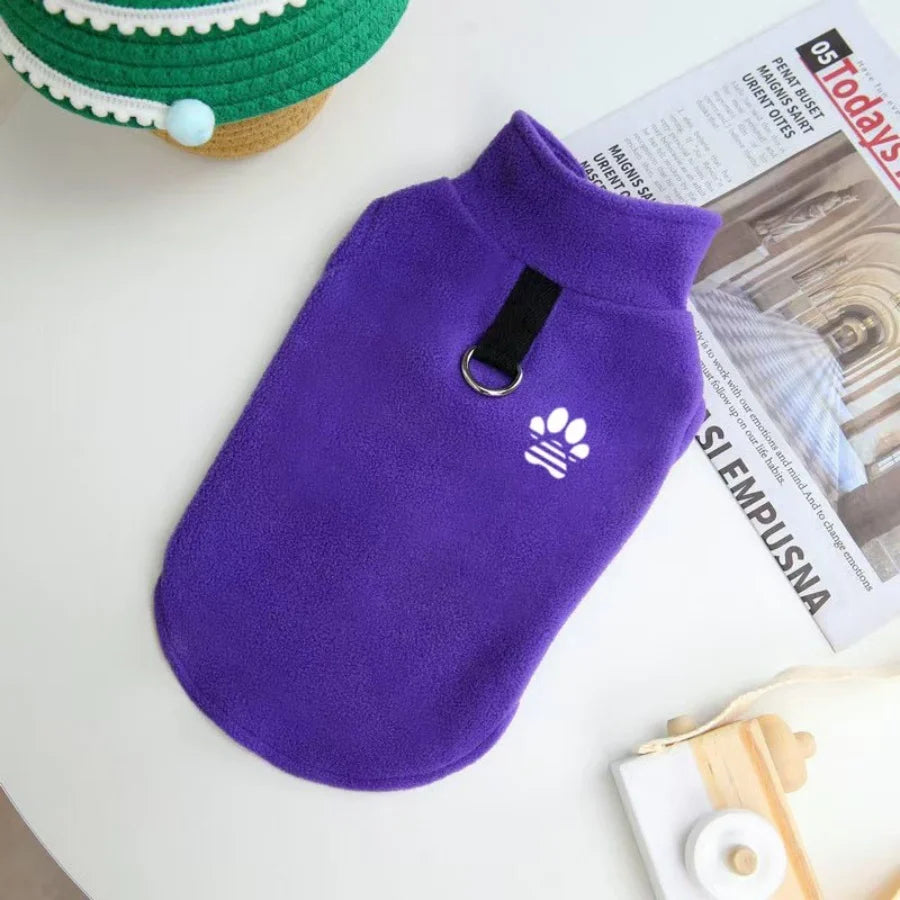 A purple fleece dog sweater with a white paw print embroidered on the chest, resting on a white surface.