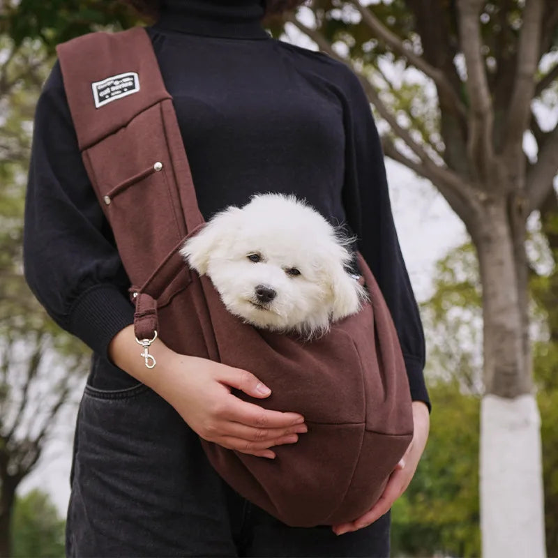A person is holding a brown portable pet carrier sling bag for cats and small dogs against a dark sweater.