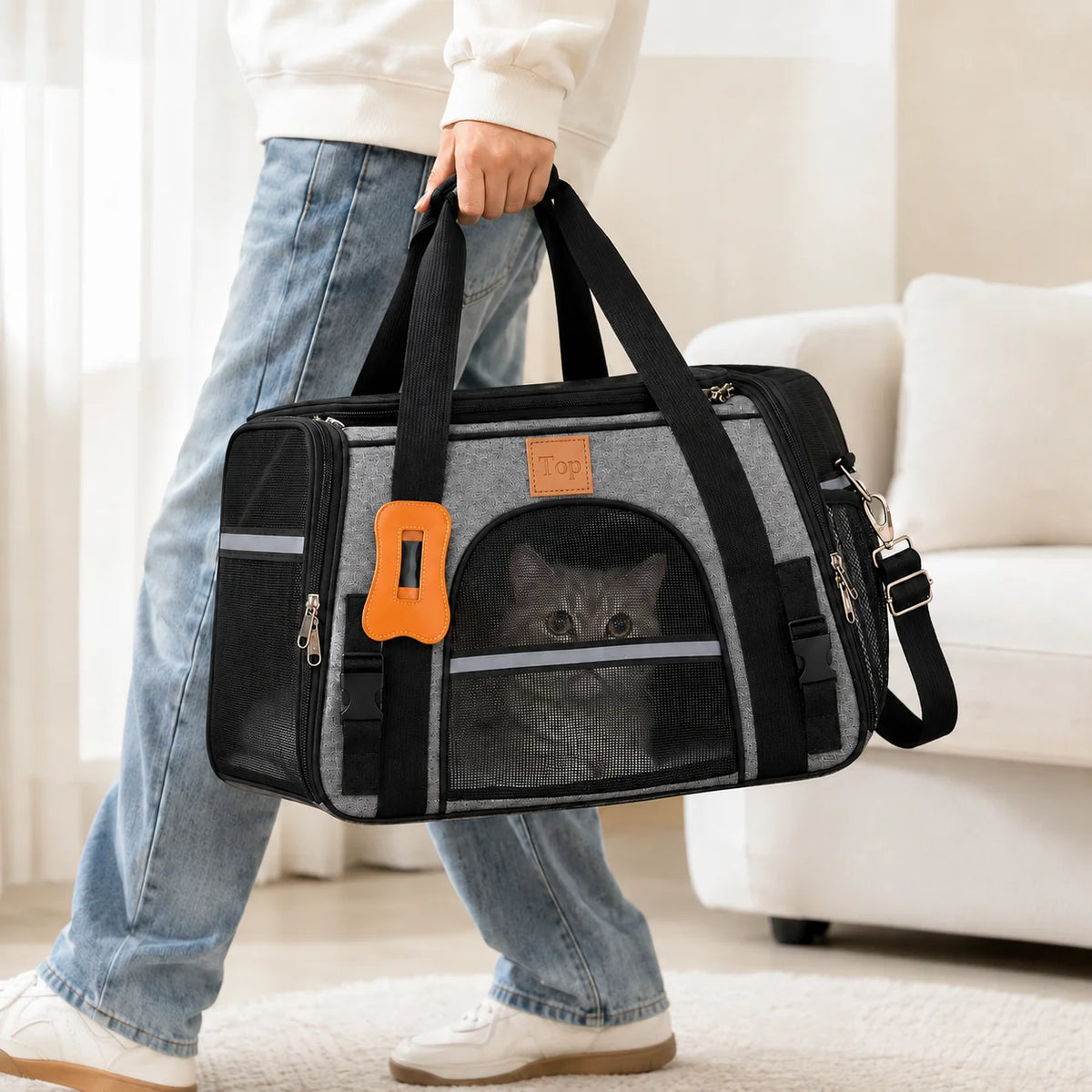 A person holds a black breathable mesh pet carrier bag with orange accents while standing indoors.