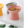 A pink ceramic food bowl filled with dry pet food sits on a white surface next to a gray bowl.
