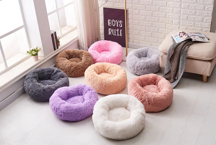 A collection of plush round pet beds in various colors including pink purple grey and beige resting on a light floor.