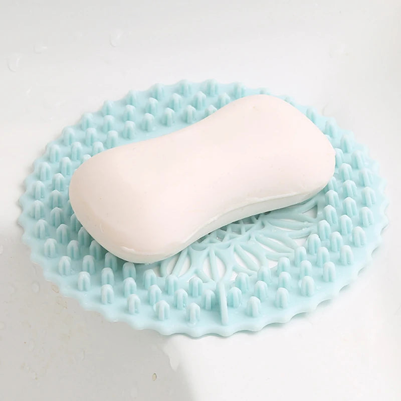 A smooth, pale pink silicone drain cover with a handle rests on a light blue textured mat.