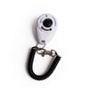 A white pet training clicker device attached to a black wrist strap.