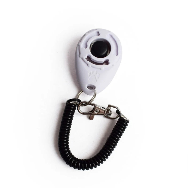 A white pet training clicker device attached to a black wrist strap.