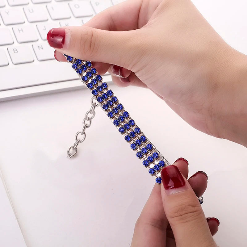 A hand is holding an elegant rhinestone pendant cat collar with a sparkling charm against a white background.