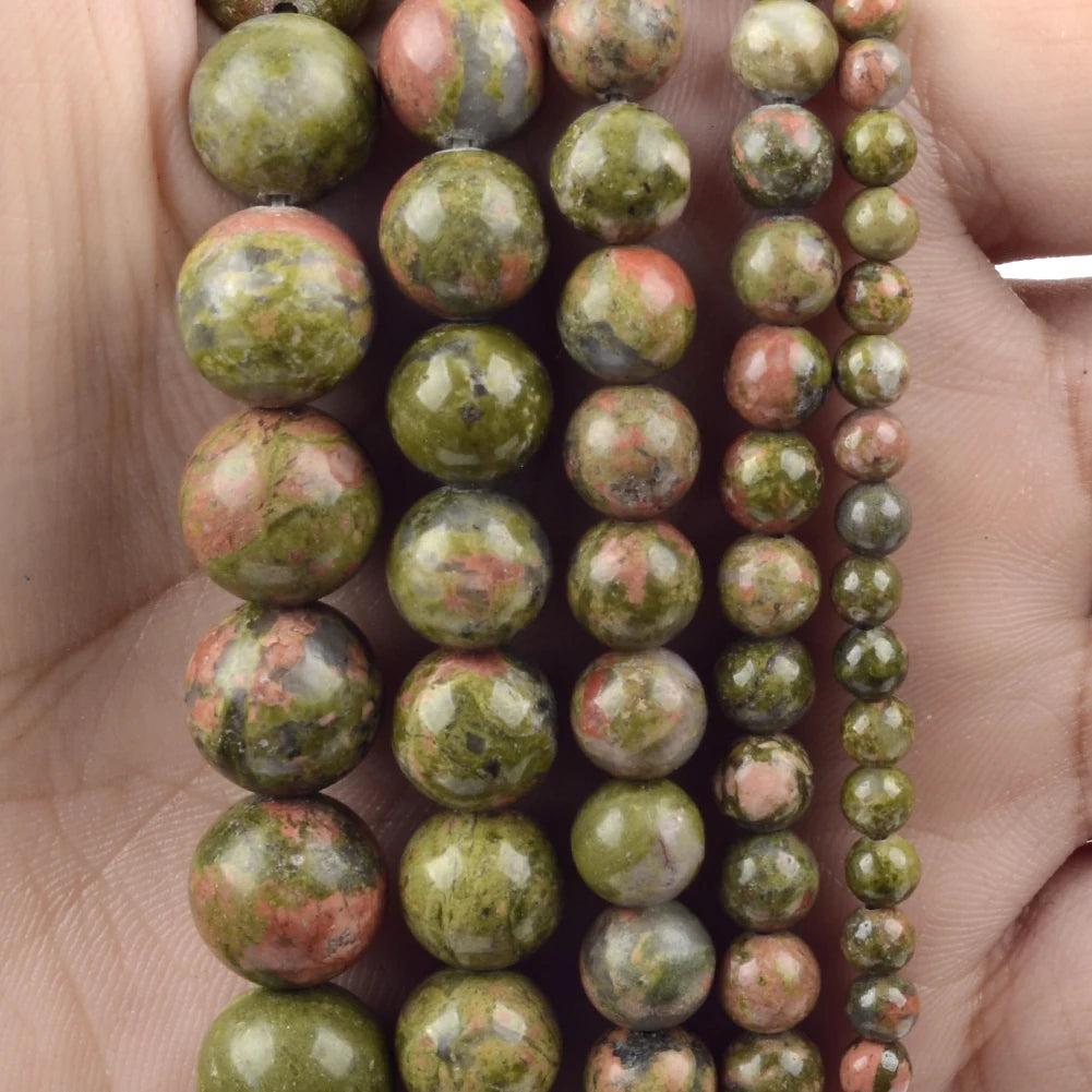 A close-up of natural stone beads in various shades of green and pink stacked on a hand.