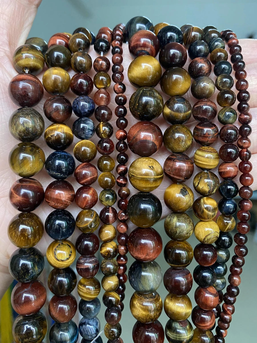 A close-up of a hand holding multiple strands of natural stone beads in various colors and sizes for jewelry making