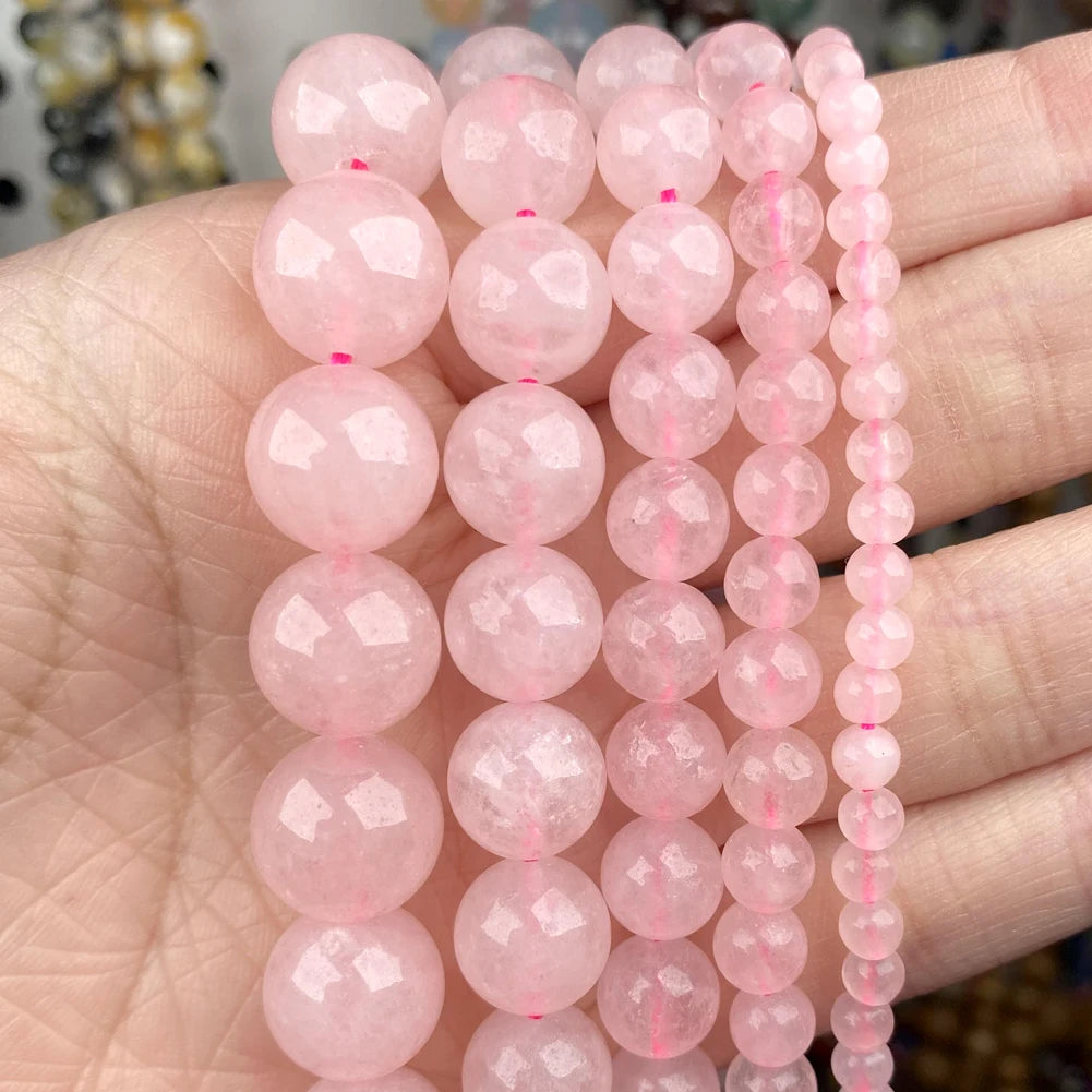 A hand holds multiple strands of pink natural stone beads for jewelry making