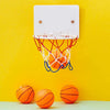An orange bouncy dog ball is placed on a light green surface against a yellow wall with a white basketball hoop.