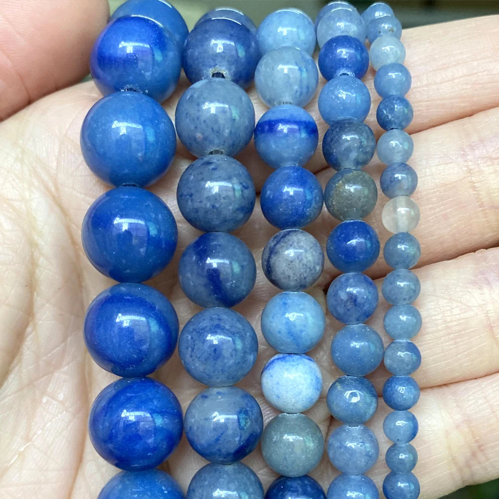 A hand holds multiple strands of natural blue and gray stone beads for jewelry making