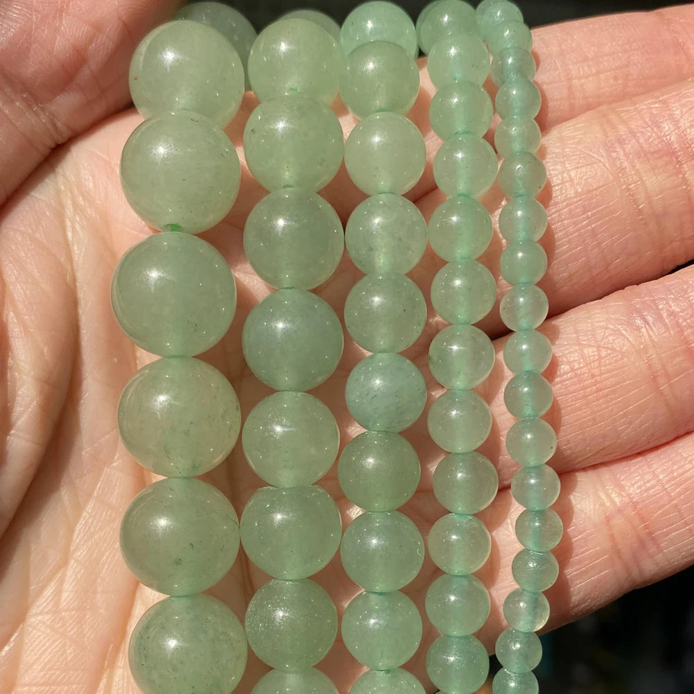 A hand holds multiple strands of light green natural stone beads for jewelry making