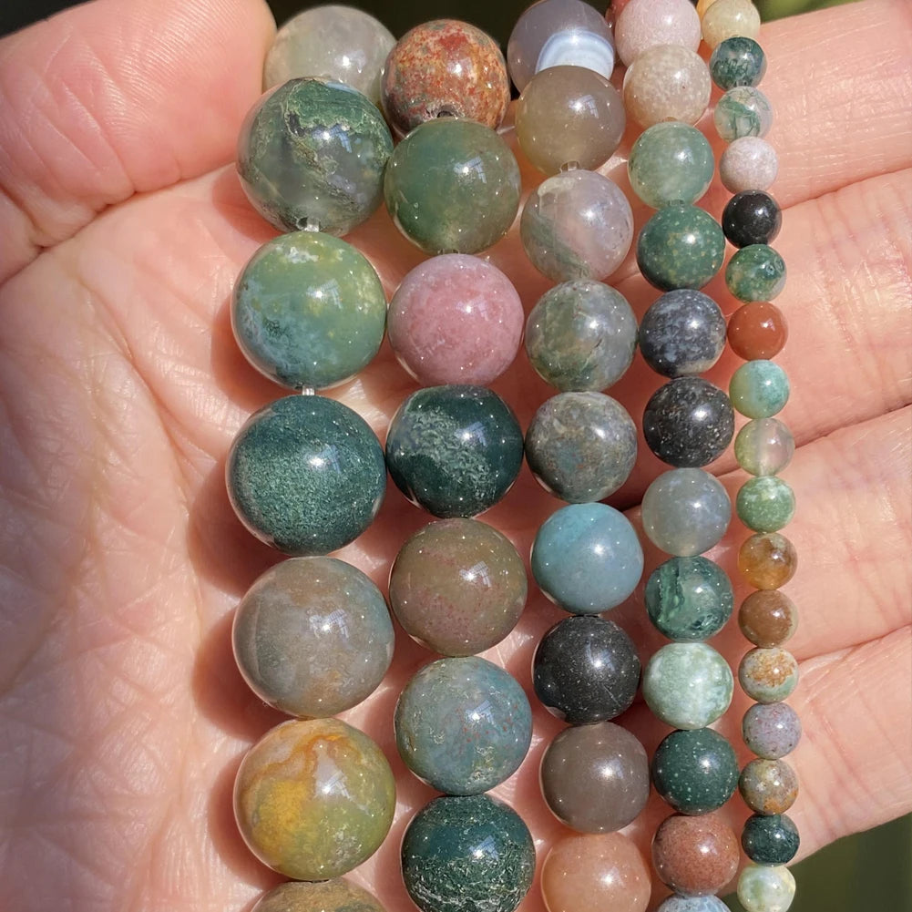 A hand holds a strand of natural stone beads in various shades of green, pink, and brown.
