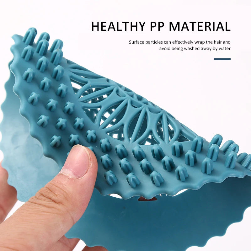 A close-up of a teal silicone drain cover with bristles and a handle being held by a hand.