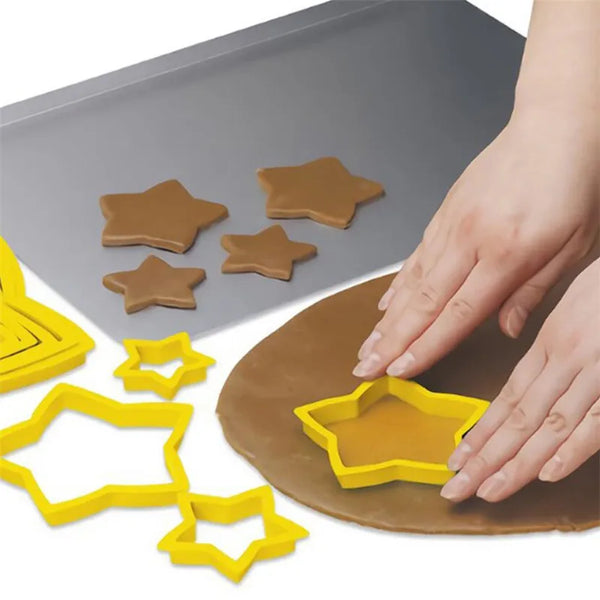 A hand is using yellow star-shaped cookie cutters on a brown dough, with a gray silicone mat nearby.