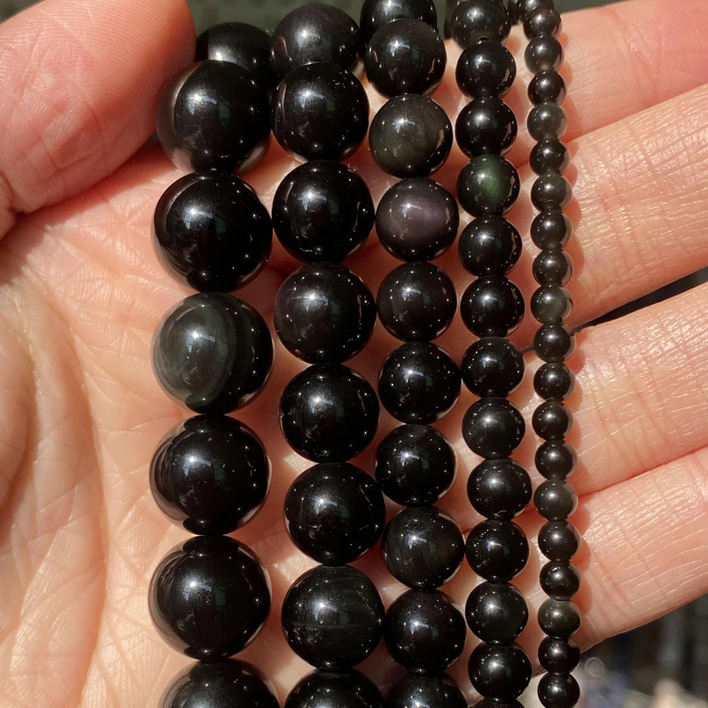 A hand holds multiple strands of dark, polished natural stone beads for jewelry making.