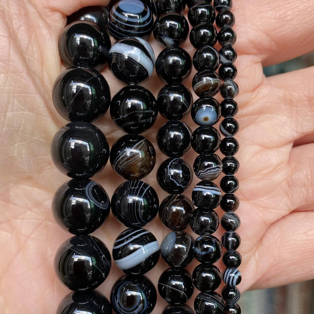A hand holds multiple strands of natural black and white marbled stone beads for jewelry making