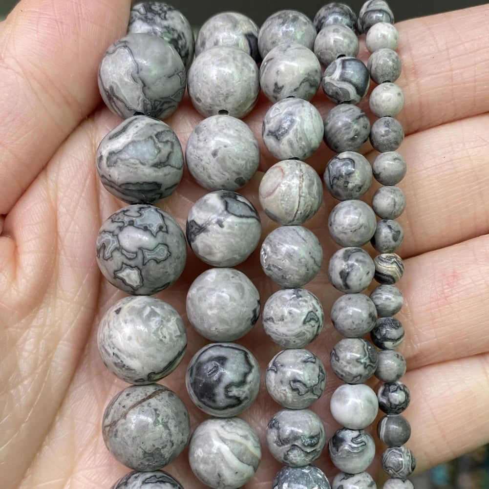 A hand holds a string of natural stone beads in various shades of gray and white for jewelry making