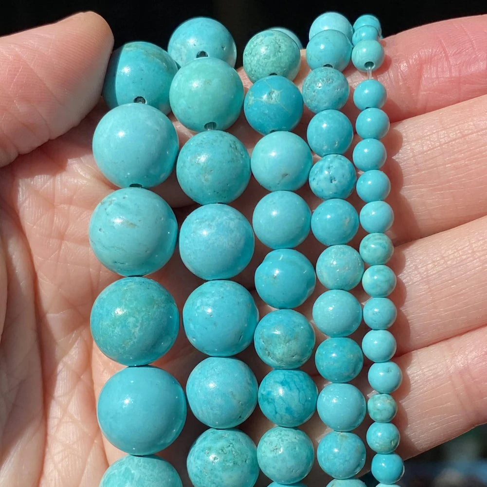 A hand holds a strand of light blue turquoise natural stone beads for jewelry making.