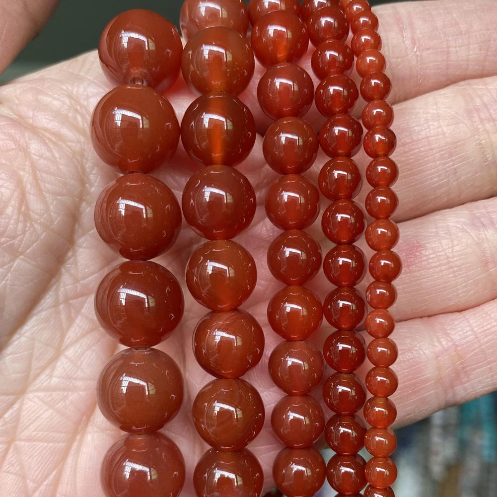 A hand holds a string of reddish-brown, polished natural stone beads for jewelry making.