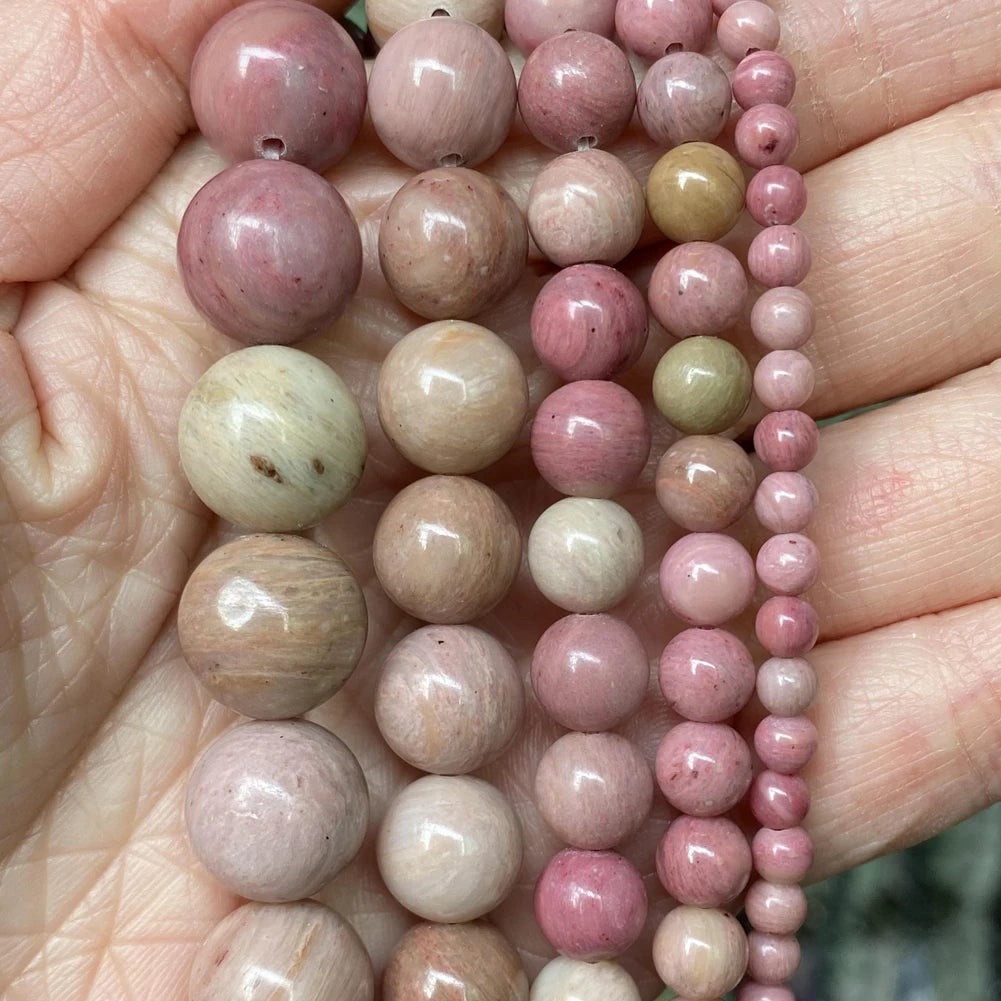 A hand holds a string of natural stone beads in various shades of pink, beige, and cream.