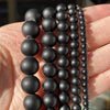 A hand holds several strands of black natural stone beads for jewelry making
