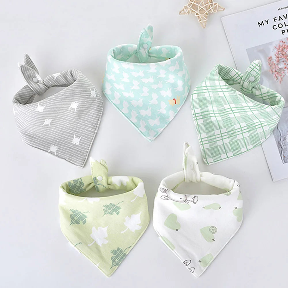 A set of five light green and white cotton triangle baby bibs with various cartoon prints displayed on a white surface.