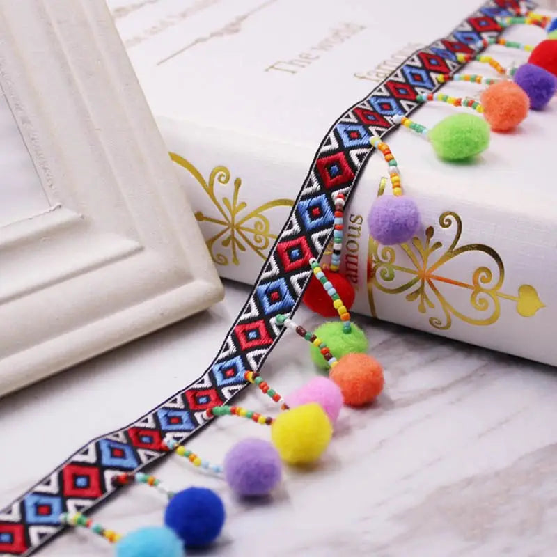 A close-up of a colorful mini pearl pom pom fringe lace trim with geometric patterns laid out on a white surface.