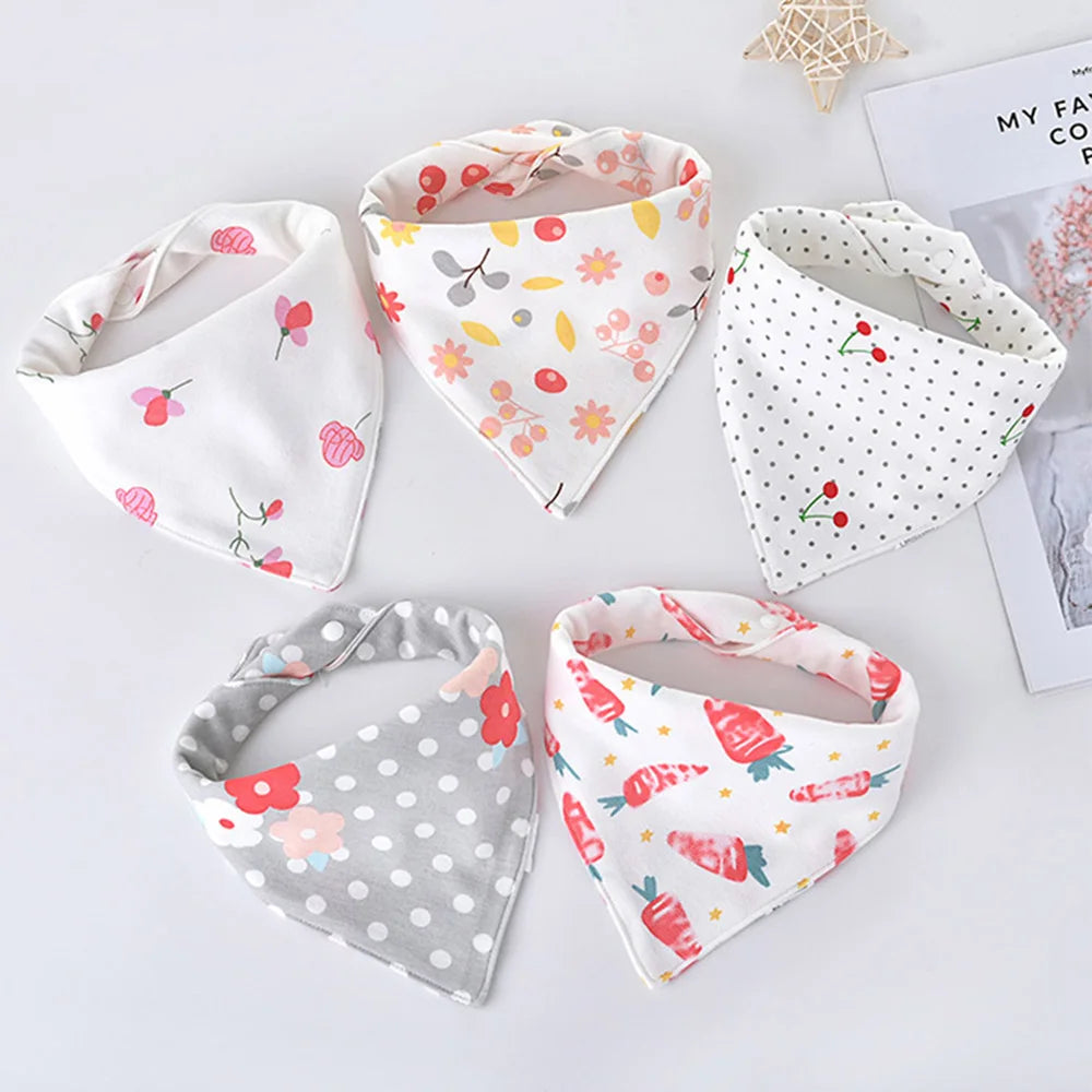 A set of five white cotton triangle baby bibs featuring various cartoon prints like strawberries and flowers.