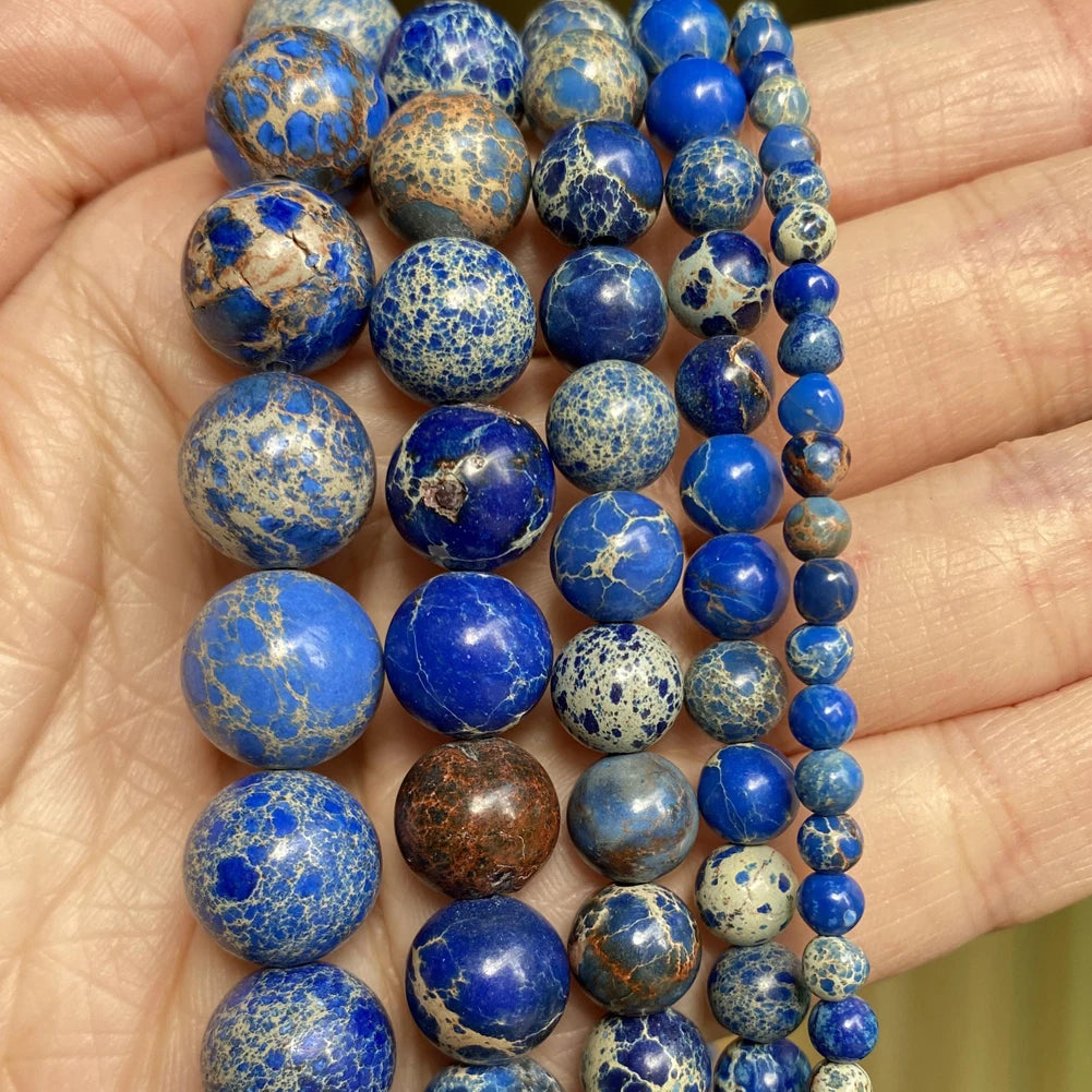 A hand holds a string of natural stone beads in various shades of blue and gray for jewelry making