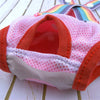 A pink and orange washable physiological dog underwear item with a rainbow-colored headband is shown on a wooden surface.
