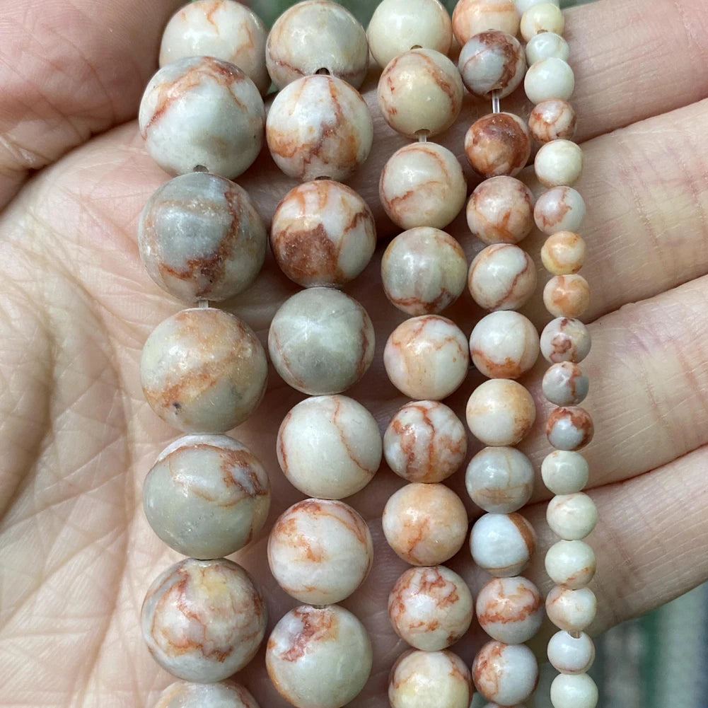 A hand holds a string of natural stone beads in various shades of beige, white, and reddish-brown for jewelry making.