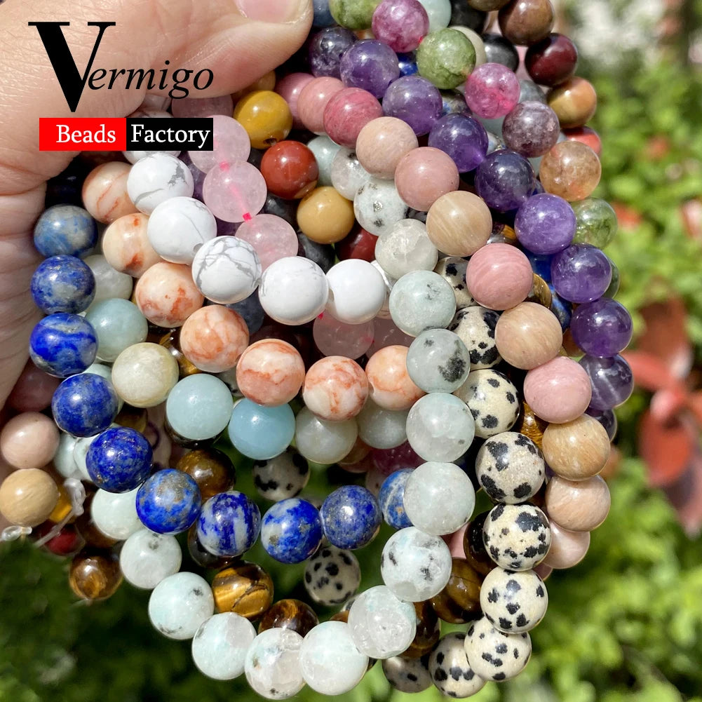 A hand holds a collection of natural stone beads in various colors and sizes for jewelry making.