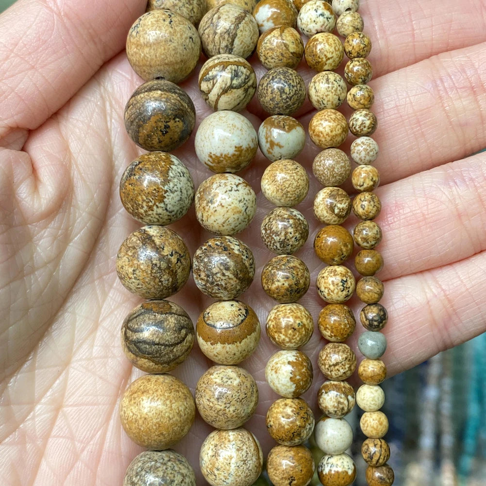 A hand holds a strand of natural stone beads in various shades of brown, beige, and cream.