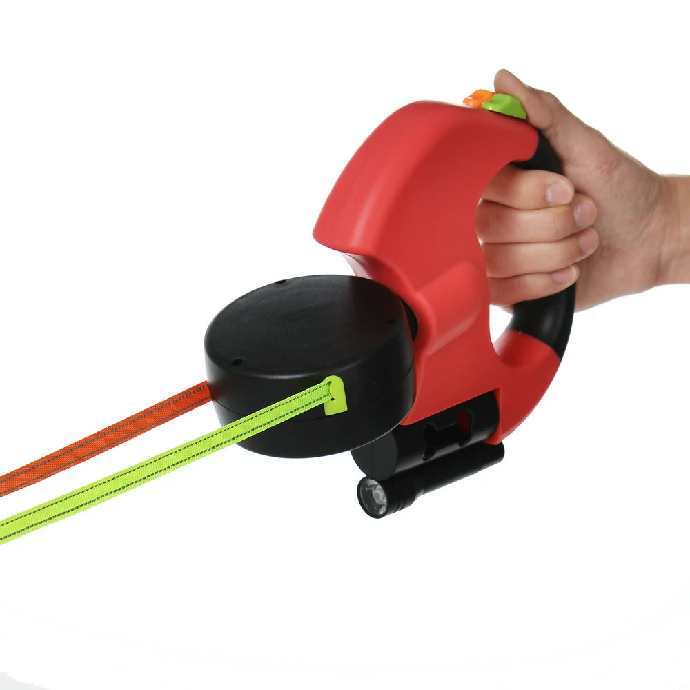 A hand holds a red retractable dog leash with a black grip and a bright yellow reflective nylon strap.