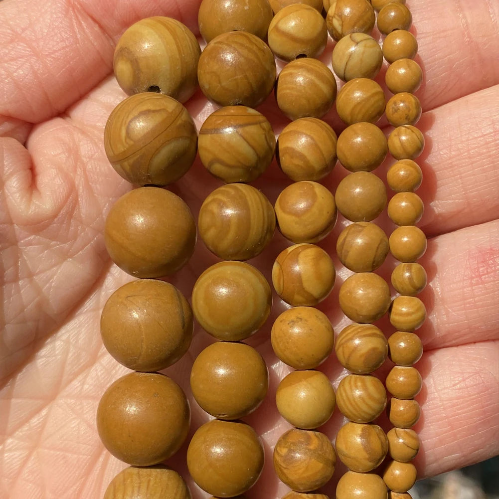 A hand holds a string of natural stone beads for jewelry making in various shades of brown and tan.
