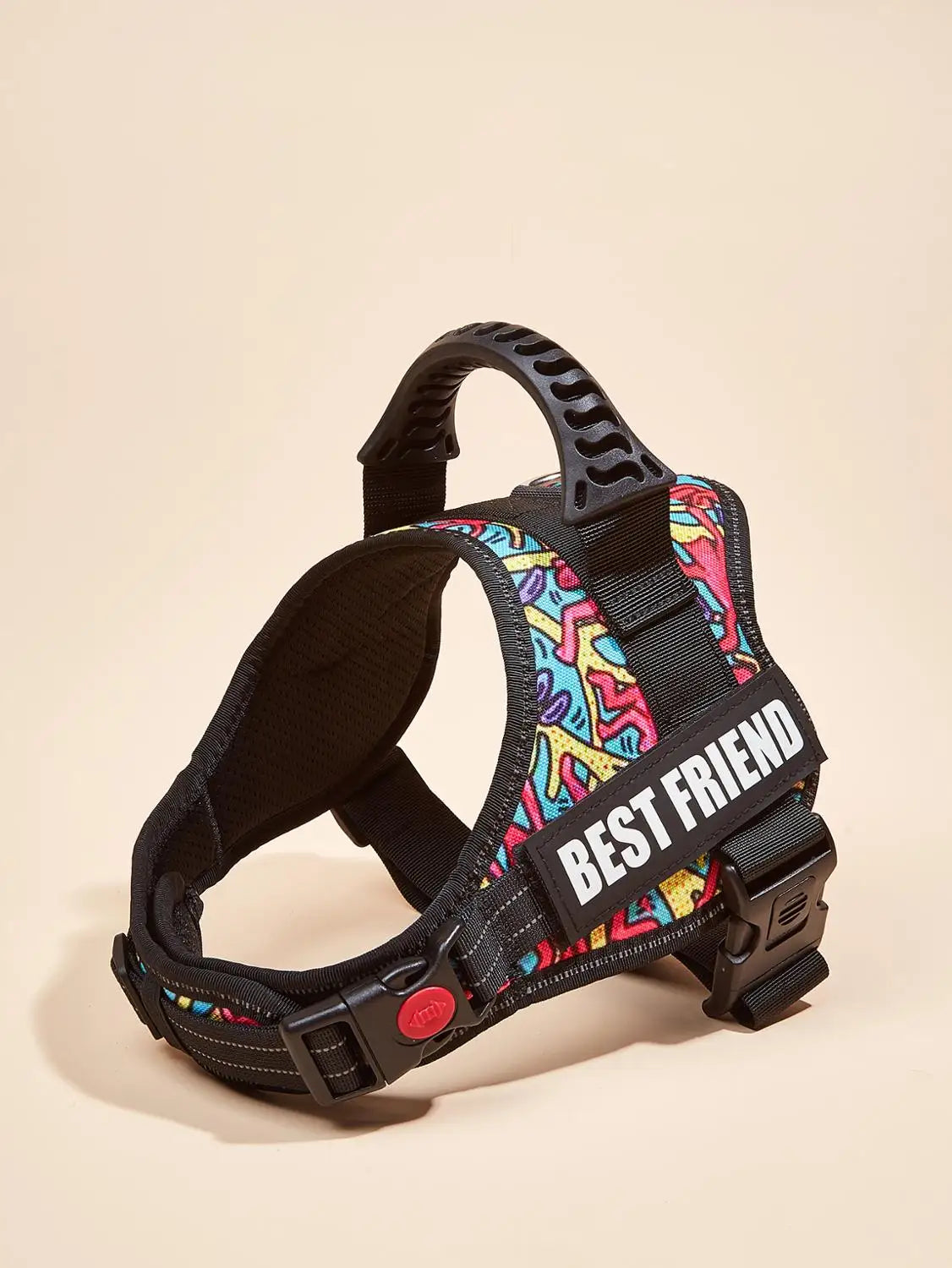A black dog harness vest with colorful patterned fabric and a white ID tag is displayed on a light background.