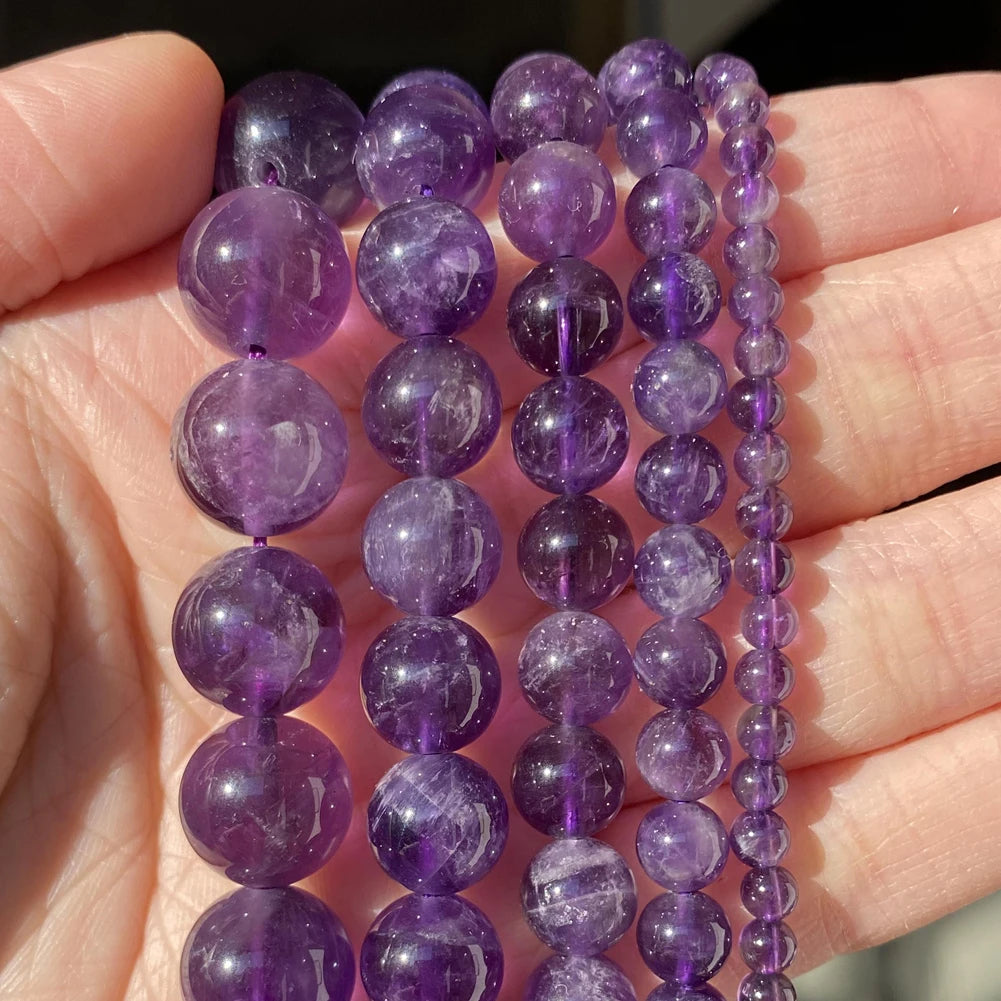A hand holds a strand of purple amethyst beads for jewelry making.