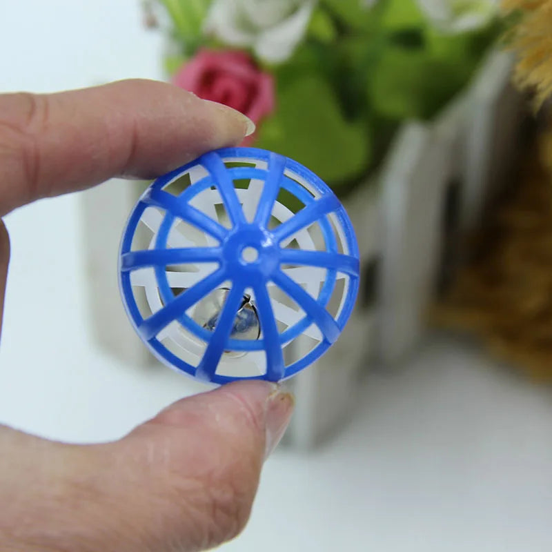 A hand holds a blue plastic cat ball toy with bells, showing its intricate mesh design.