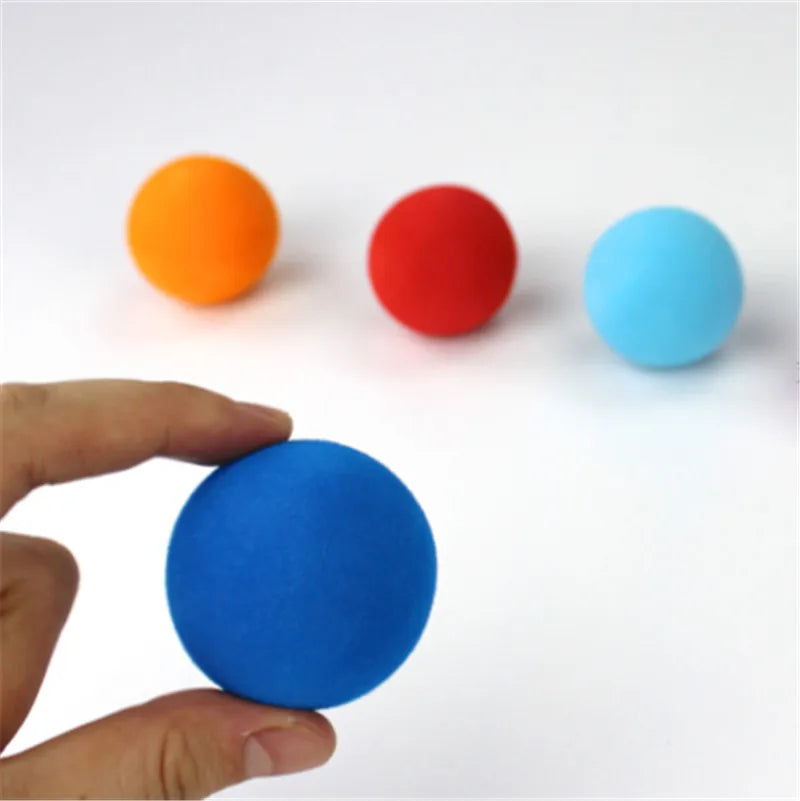 A hand holds a blue foam golf ball next to three other colored balls: orange, red, and light blue.