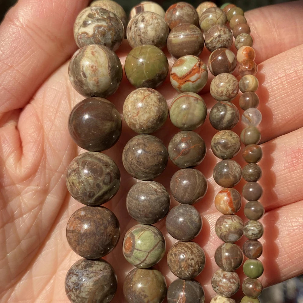 A hand holds a string of natural stone beads in various shades of brown, green, and beige for jewelry making.