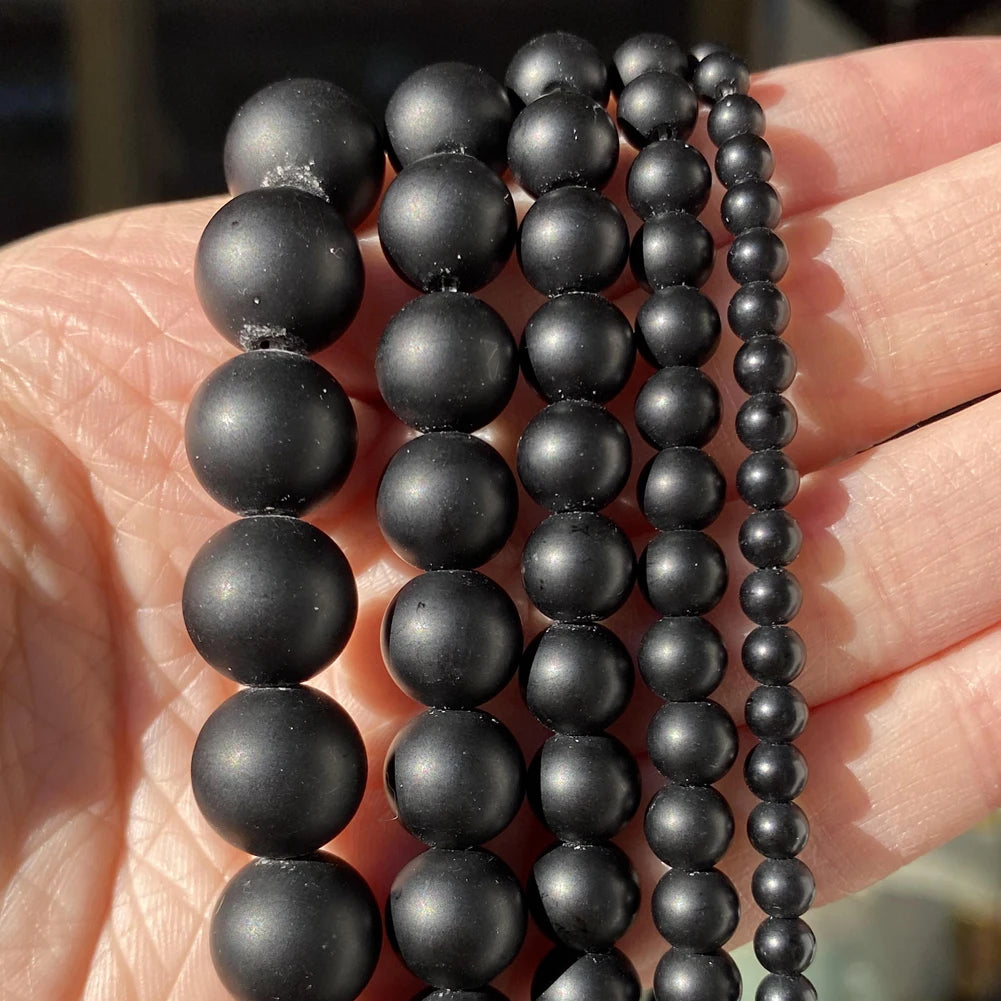 A hand holds several strands of black natural stone beads for jewelry making